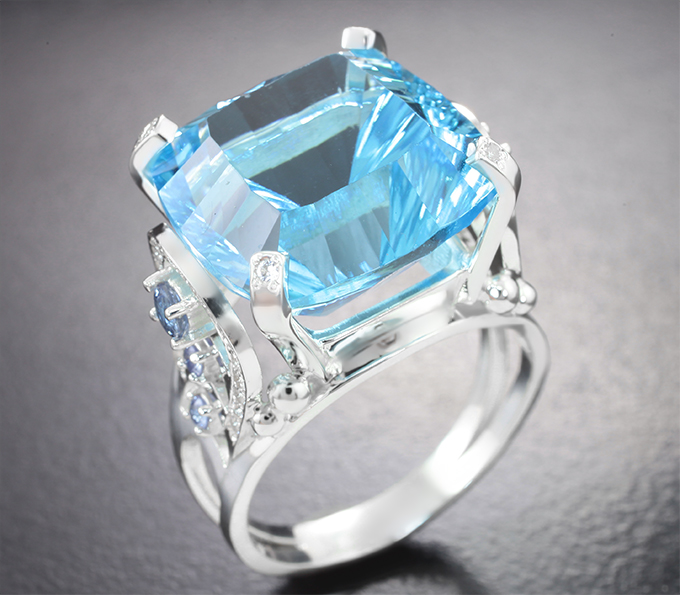 Золото Кольцо с голубым топазом авторской огранки 20,99 карата, голубыми сапфирами и бесцветными цирконами